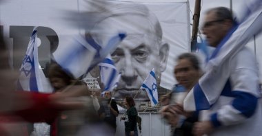 Demonstrators walk with Israel's national flags next to a banner showing Prime Minister Benjamin Netanyahu during a protest against plans by his government to overhaul the judicial system in Tel Aviv, Israel, March 25, 2023. (AP Photo)