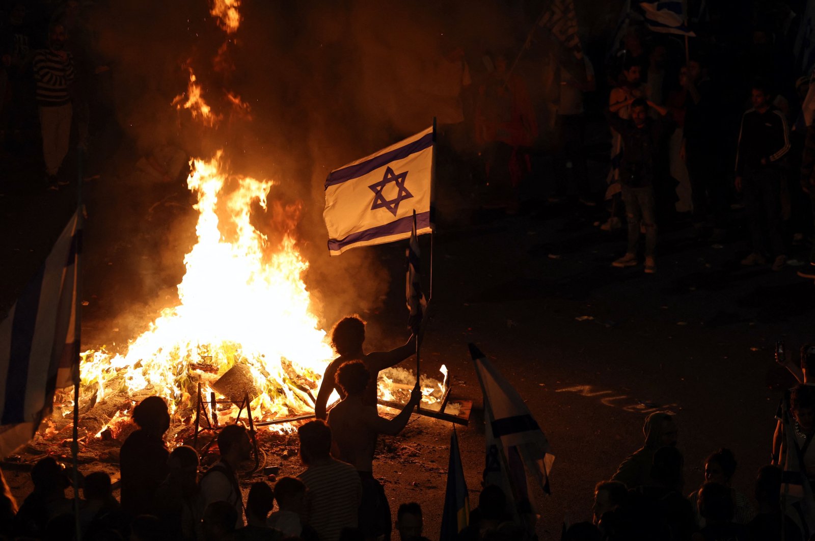 Protesters hold an Israeli flag as they gather around a bonfire during an anti-government rally, Tel Aviv, Israel, March 27, 2023. (AFP Photo)