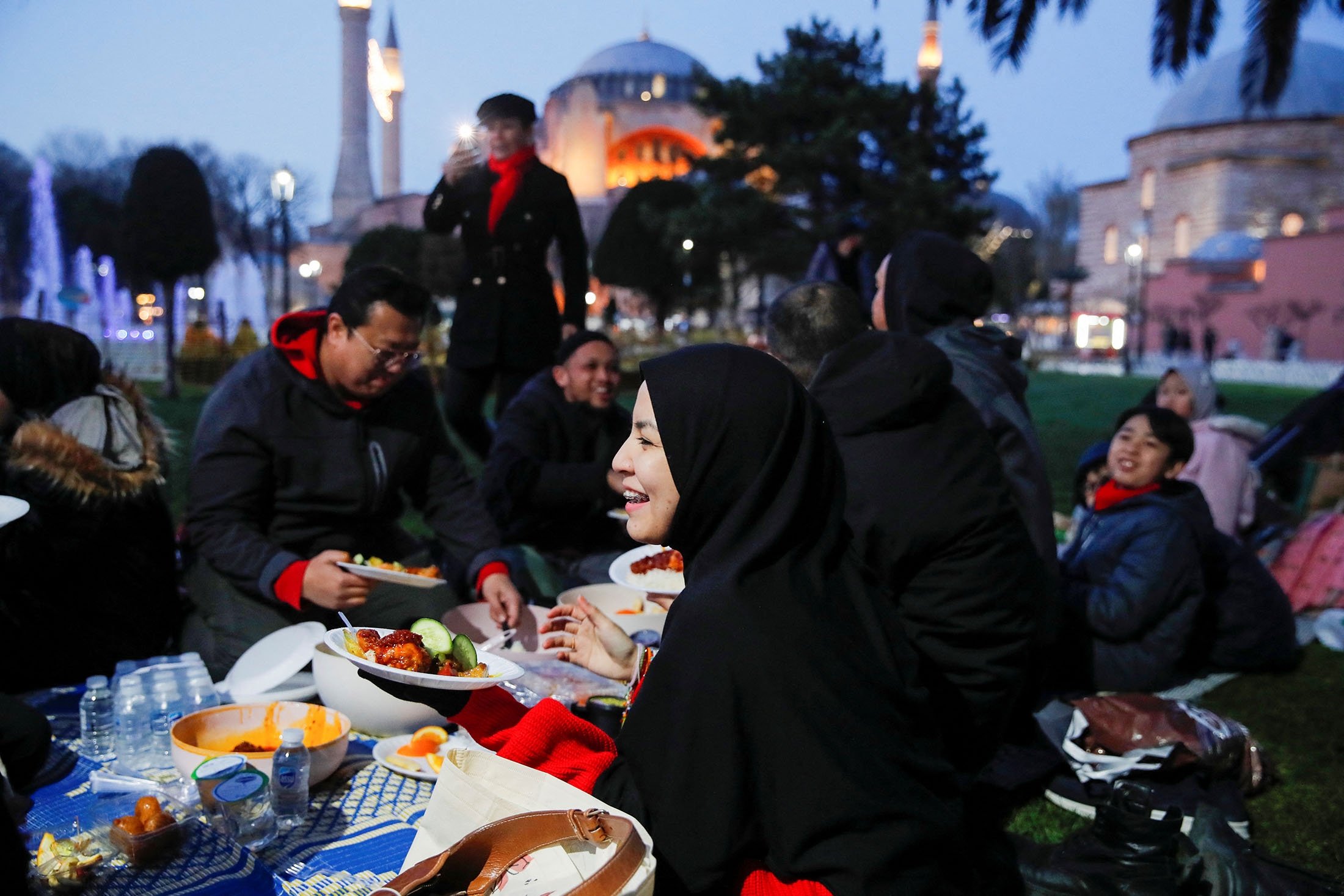 Orang-orang, dengan Masjid Agung Hagia Sophia sebagai latar belakang, berbuka puasa, atau berbuka puasa, di Lapangan Sultanahmet pada hari pertama bulan suci Ramadhan di Istanbul, Türkiye, 23 Maret 2023. (Foto Reuters)