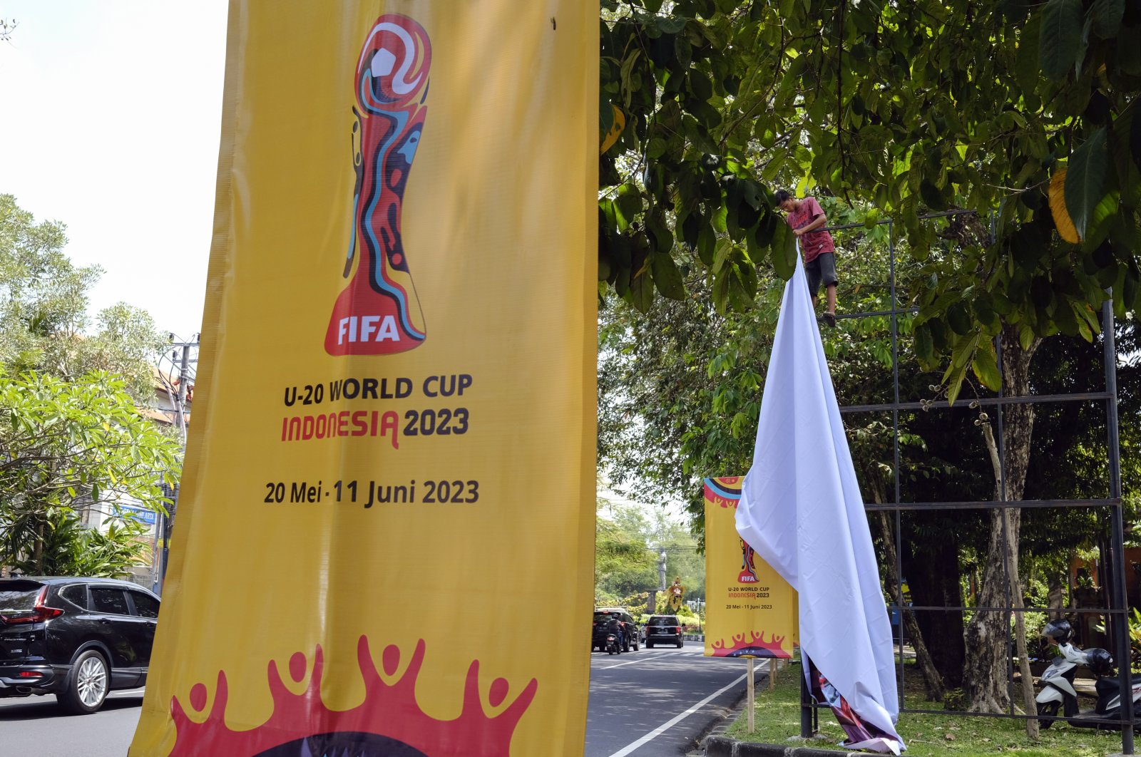 A worker removes a banner of FIFA U-20 World Cup 2023 at a main road, Denpasar, Bali, Indonesia, March 27, 2023. (EPA Photo)