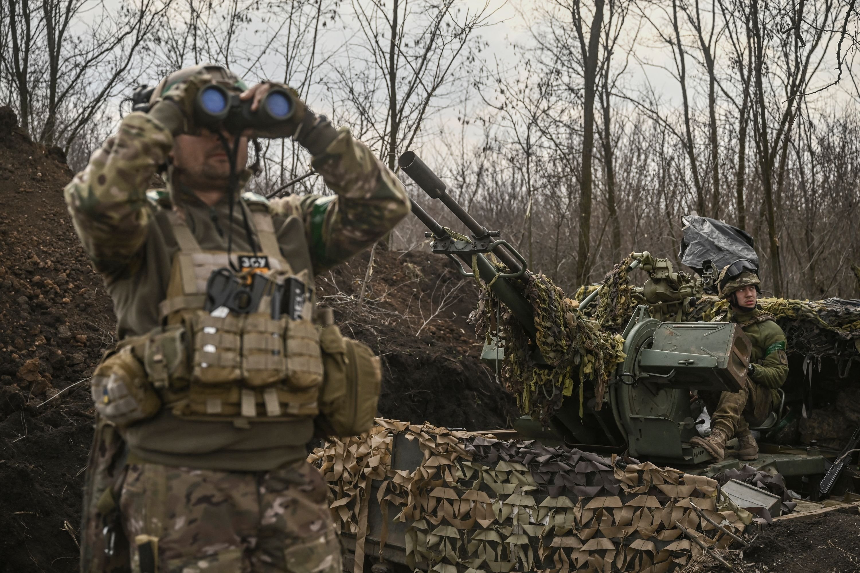 Seorang prajurit Ukraina (kiri) melihat dengan teropong di sebelah yang lain (kanan) duduk di atas senjata anti-udara di dekat Bakhmut, Ukraina, 24 Maret 2023. (Foto AFP)