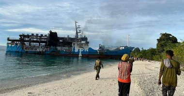 People walking toward the burnt passenger ferry, Basilan province, southern Philippines, March 30, 2023. (AFP Photo)