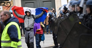 A protester holds a French flag as he walks in front of a line of gendarmes in riot gear during a demonstration after the government pushed a pensions reform through parliament without a vote, Paris, France, March 28, 2023. (AFP Photo)