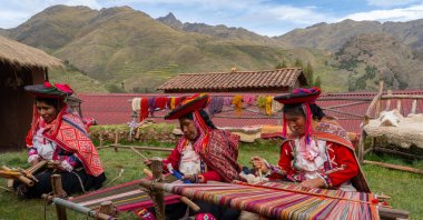 Three local female weavers, in colorful traditional local dress including festooned hats, weave colorful alpaca wool, Peru. (Getty Images Photo)