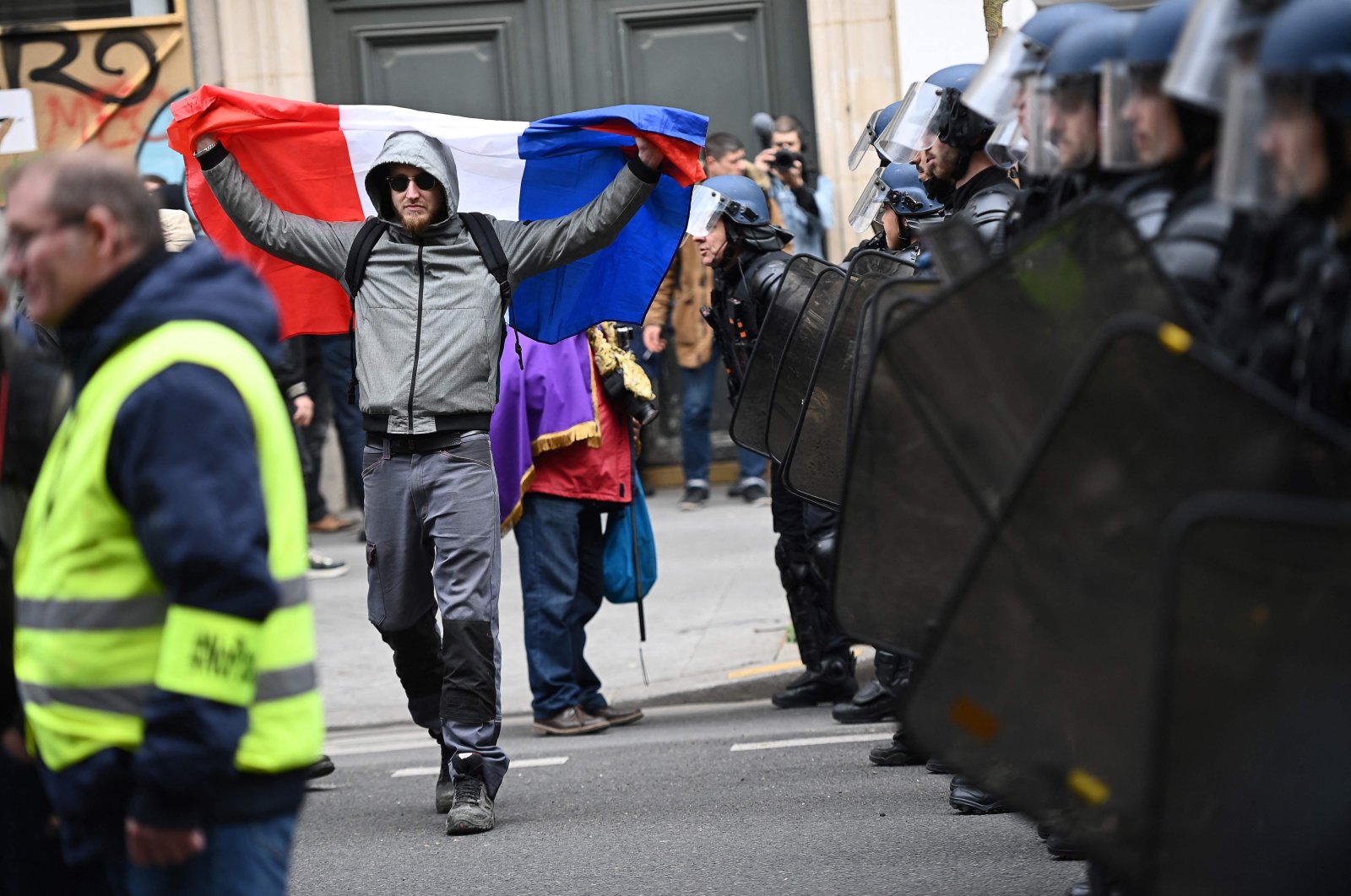 A protester holds a French flag as he walks in front of a line of gendarmes in riot gear during a demonstration after the government pushed a pensions reform through parliament without a vote, Paris, France, March 28, 2023. (AFP Photo)