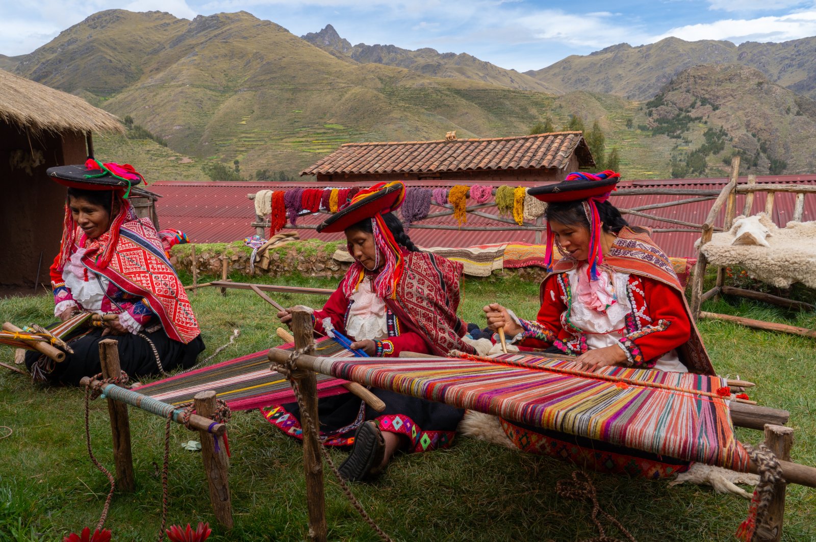 Three local female weavers, in colorful traditional local dress including festooned hats, weave colorful alpaca wool, Peru. (Getty Images Photo)