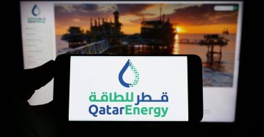 A person holds a mobile phone with the logo of Qatari petroleum company QatarEnergy on screen in front of a business website in Stuttgart, Germany, Sept. 10, 2022. (Shutterstock Photo)