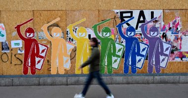 A pedestrian passes by posters of anti-riot policemen ahead of a demonstration on the 11th day of action after the government pushed a pensions reform through parliament without a vote, using Article 49.3 of the constitution, in Rennes, western France, April 6, 2023. (AFP Photo)