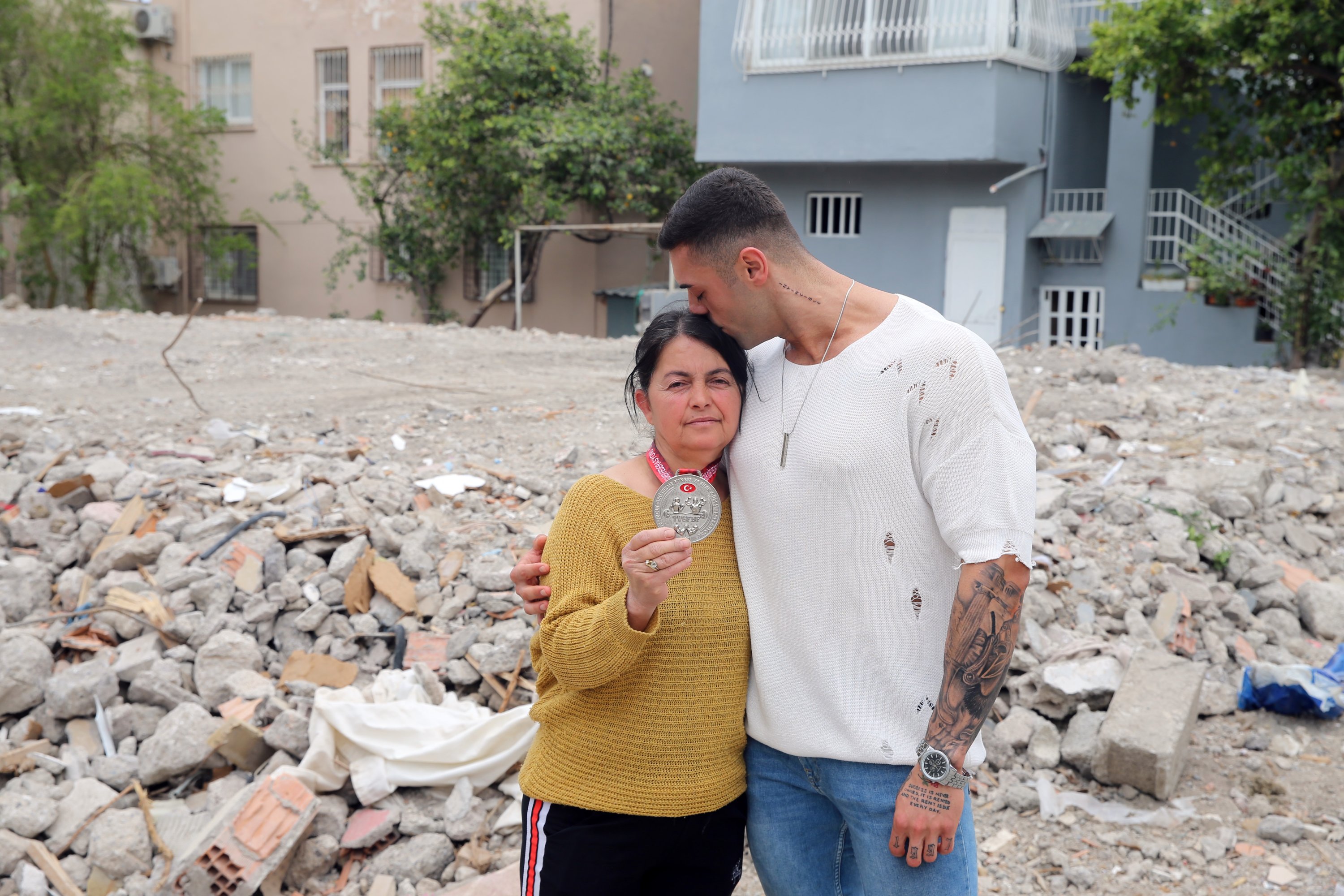 Barış Üstün (kanan) bersama ibunya yang menunjukkan medali perak Kejuaraan Binaraga dan Kebugaran Türkiye di depan rumah mereka yang hancur, Hatay, Türkiye, 10 April 2023. (Foto AA)