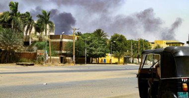 Smoke rises from buildings as a tuktuk taxi driver sits in his vehicle along a deserted street in Khartoum, Sudan, April 16, 2023. (AFP Photo)