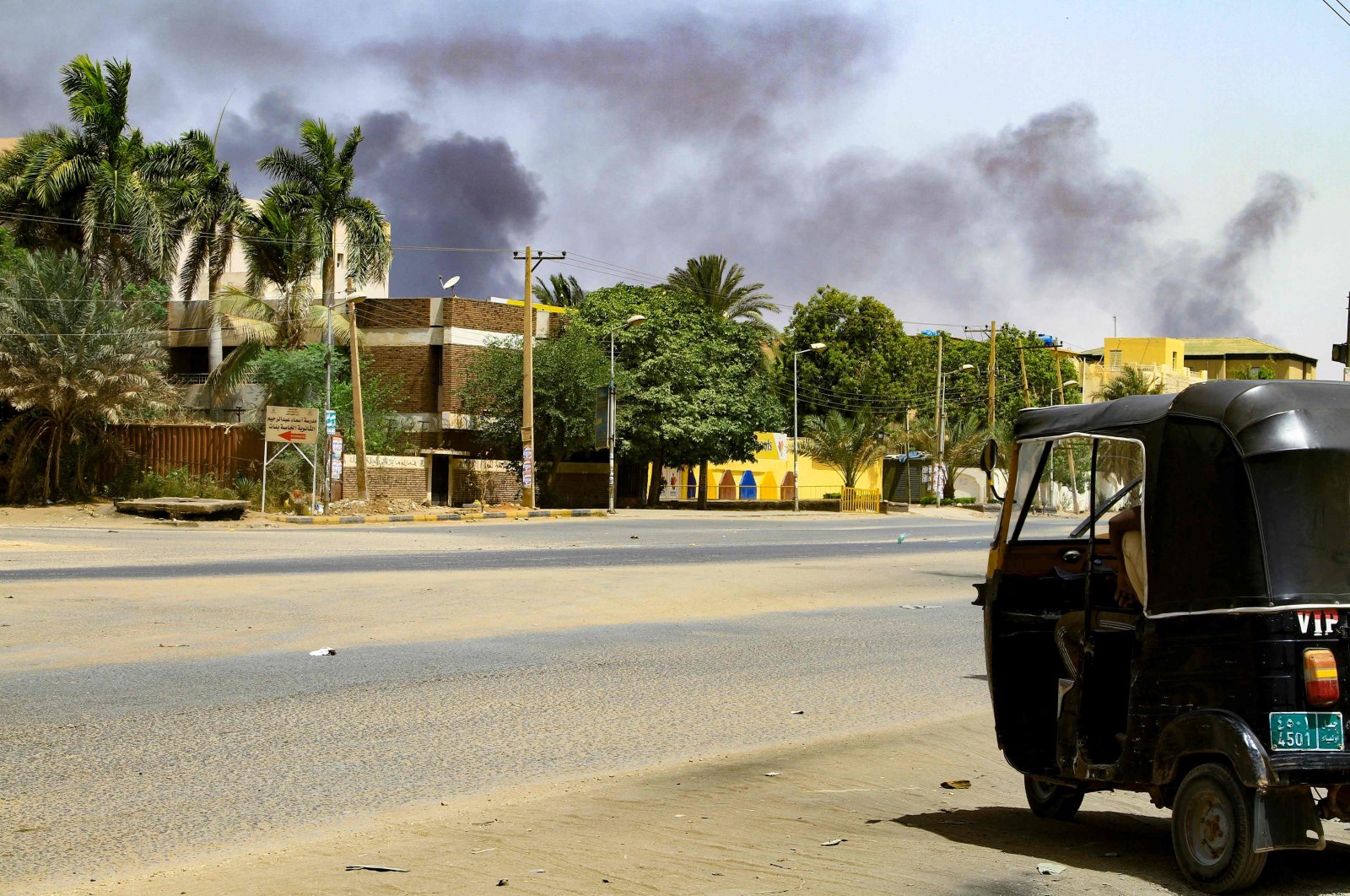 Smoke rises from buildings as a tuktuk taxi driver sits in his vehicle along a deserted street in Khartoum, Sudan, April 16, 2023. (AFP Photo)