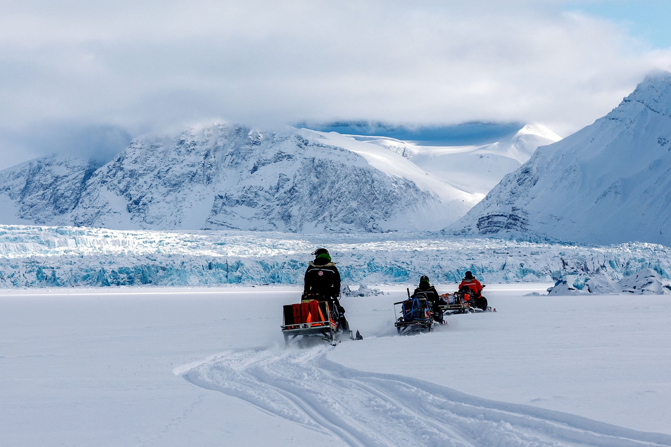 Para ilmuwan mengendarai mobil salju mereka di dekat gletser Kronebreen melalui lanskap Arktik dekat Ny-Alesund, Svalbard, Norwegia, 10 April 2023. (Foto Reuters)