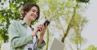 Young woman is seen using mobile phone, holding laptop in this undated photo. (Shutterstock Photo)