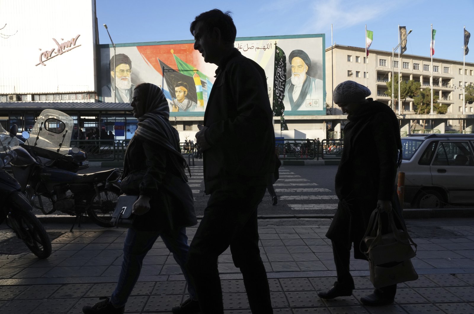 Pedestrians walk on a sidewalk in front of a mural showing the late Iranian revolutionary founder Ayatollah Khomeini, right, Supreme Leader Ayatollah Ali Khamenei, left, and Basij paramilitary force, at Enqelab-e-Eslami (Islamic Revolution) street, in downtown Tehran, Iran, Saturday, Jan. 7, 2023. (AP File Photo)