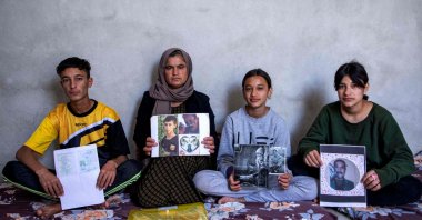 Bahar Elias, a 40-year-old displaced Iraqi woman from the Yazidi community, poses for a picture with her son and daughters while holding pictures of other family members kidnapped by Daesh, during an interview at the Sharya camp near Dohuk city in northern Iraq, April 22, 2023. (AFP Photo)