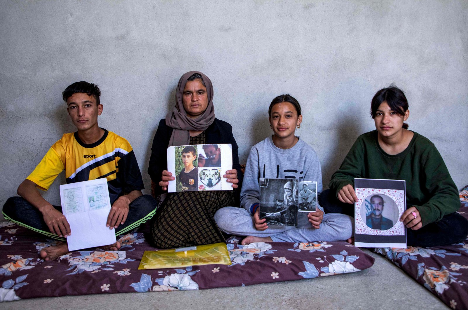 Bahar Elias, a 40-year-old displaced Iraqi woman from the Yazidi community, poses for a picture with her son and daughters while holding pictures of other family members kidnapped by Daesh, during an interview at the Sharya camp near Dohuk city in northern Iraq, April 22, 2023. (AFP Photo)