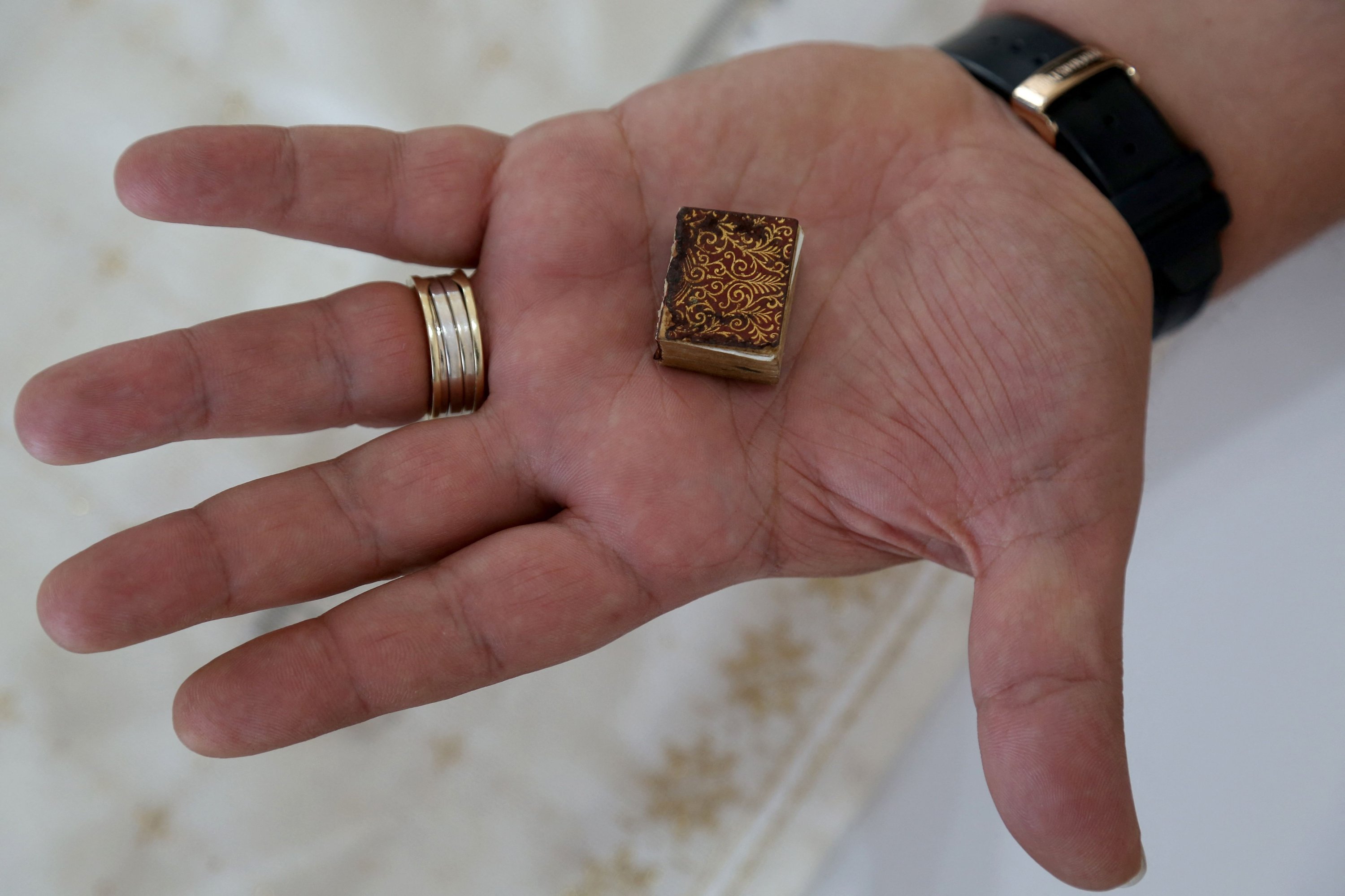 Mario Prushi memegang salah satu Alquran terkecil, berukuran prangko dengan sampul yang dibuat dari beludru bersulam emas, di Tirana, Albania, 17 April 2023. (Foto AFP)