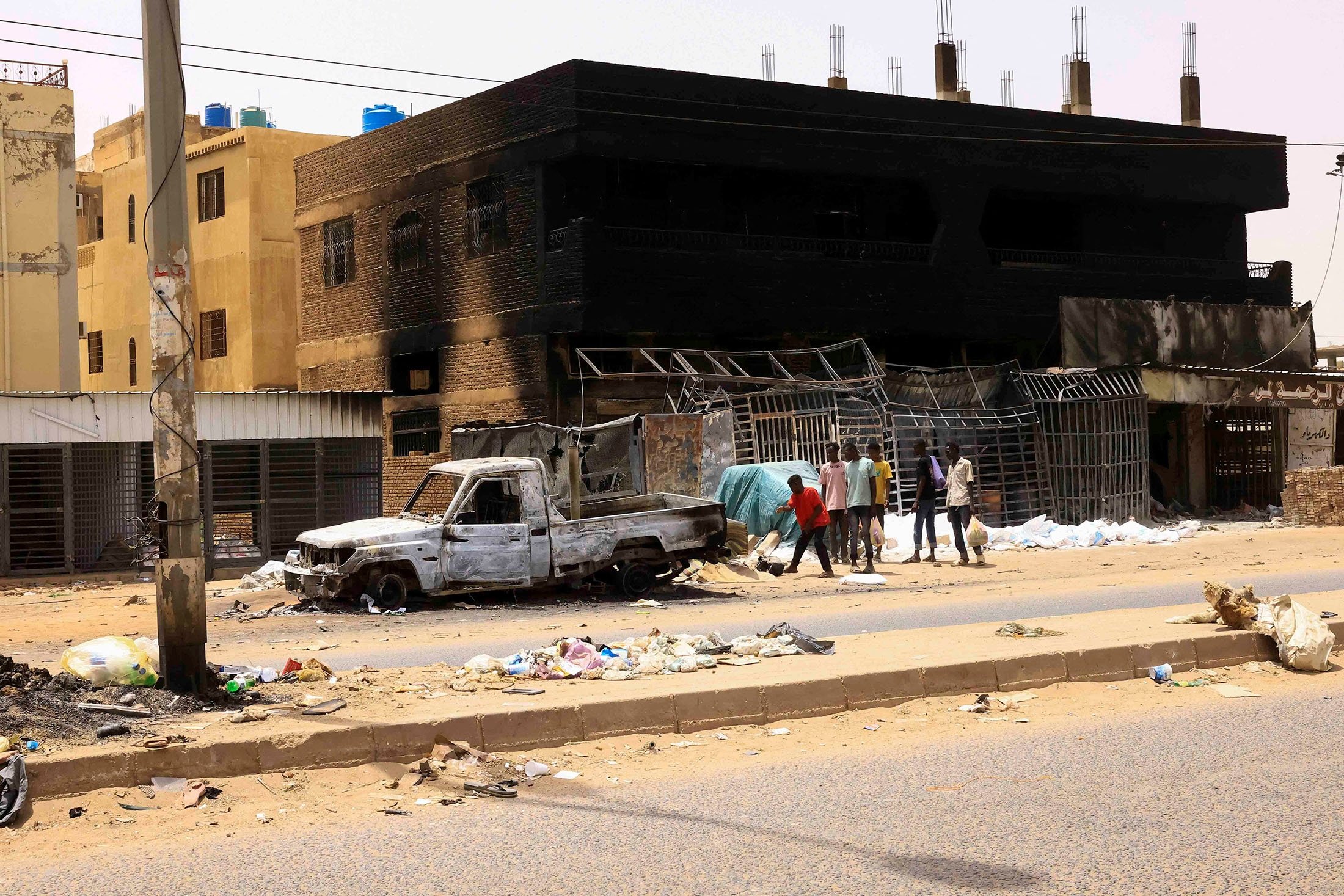 People walk near damaged car and buildings at the central market during clashes between the paramilitary Rapid Support Forces and the army in Khartoum, Sudan, April 27, 2023. (Reuters Photo)
