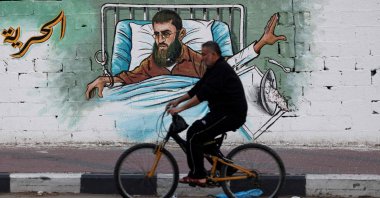 A Palestinian man rides his bike past a mural depicting Khader Adnan in Gaza City, Palestine, May 2, 2023. (AFP Photo)