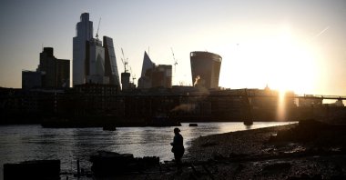 A person stands on the bank of the River Thames during sunrise, with the City of London financial district in the background, in London, Britain, April 4, 2023. (Reuters Photo)