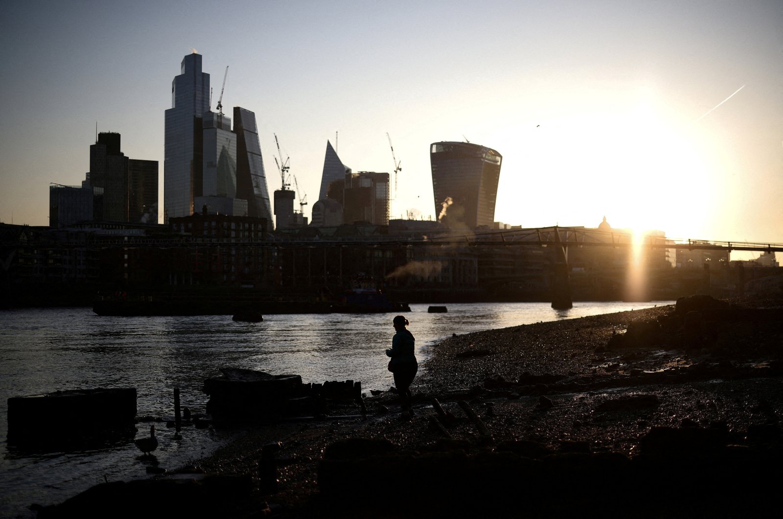 A person stands on the bank of the River Thames during sunrise, with the City of London financial district in the background, in London, Britain, April 4, 2023. (Reuters Photo)