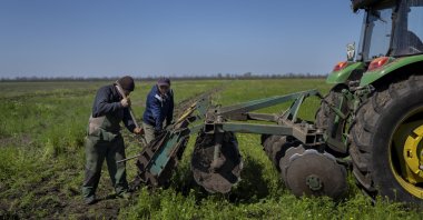 Two farmers remove mud from a tractor as they try to harvest a field in Potomkyne, Kherson region, Ukraine, April 25, 2023. (AP Photo)