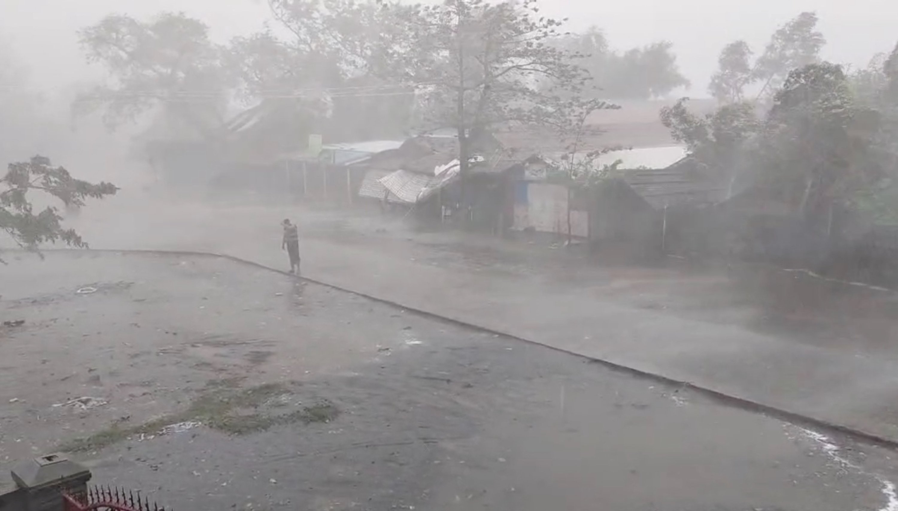 Tangkapan layar yang diambil dari video selebaran menunjukkan seorang pria berdiri saat angin kencang dan hujan lebat di kamp ThekayPyin Rohingya, saat Topan Mocha mendekat, di Sittwe, Rakhine, Myanmar, 14 Mei 2023. (Foto Reuters)