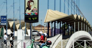A couple ride a Vespa motorcycle past a street thermometer reading 44 degrees Celsius in Seville, Spain, April 26, 2023. (AFP Photo)