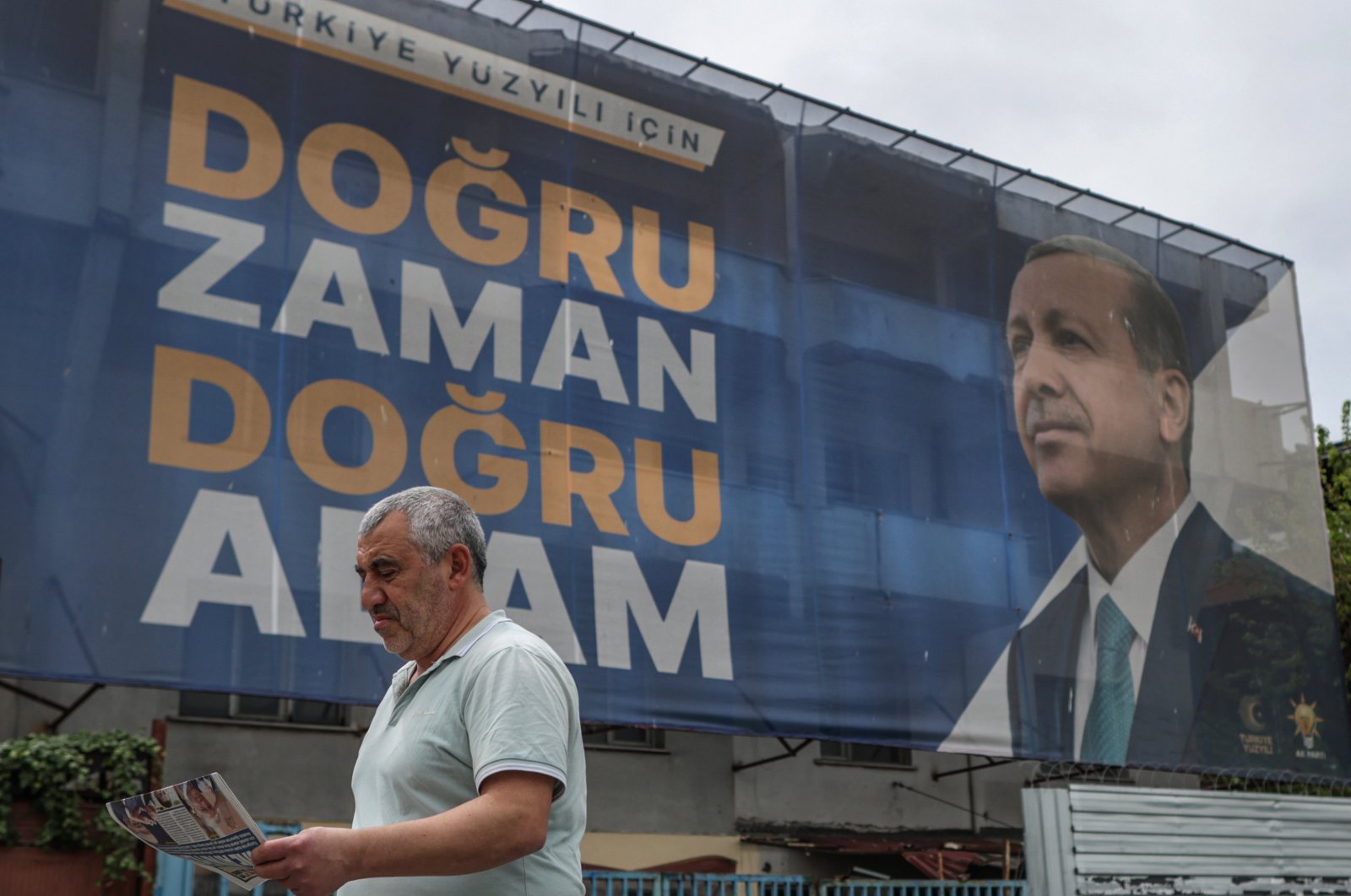 A man walks and reads a newspaper in front of an election campaign poster of Turkish President Recep Tayyip Erdoğan on the day after the general elections in Istanbul, Türkiye, May 15, 2023. (EPA Photo)
