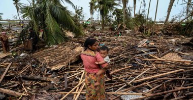 A Rohingya woman carries her baby next to her destroyed house at Basara refugee camp in Sittwe, Myanmar, May 16, 2023. (AFP Photo)