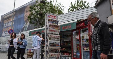 A street vendor looks at newspapers in stall next to an election campaign poster of President Recep Tayyip Erdoğan on the day after the general elections in Istanbul, Türkiye, May 15, 2023. (EPA Photo)