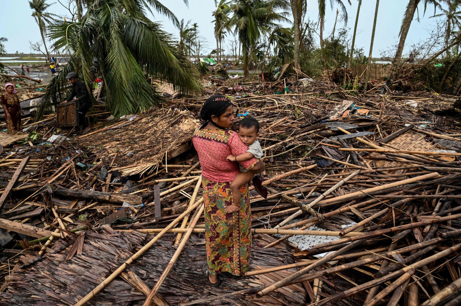 A Rohingya woman carries her baby next to her destroyed house at Basara refugee camp in Sittwe, Myanmar, May 16, 2023. (AFP Photo)