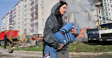 A woman walks past damaged residential buildings as she carries a child in Uman, Ukraine, April 28, 2023. (AFP Photo)