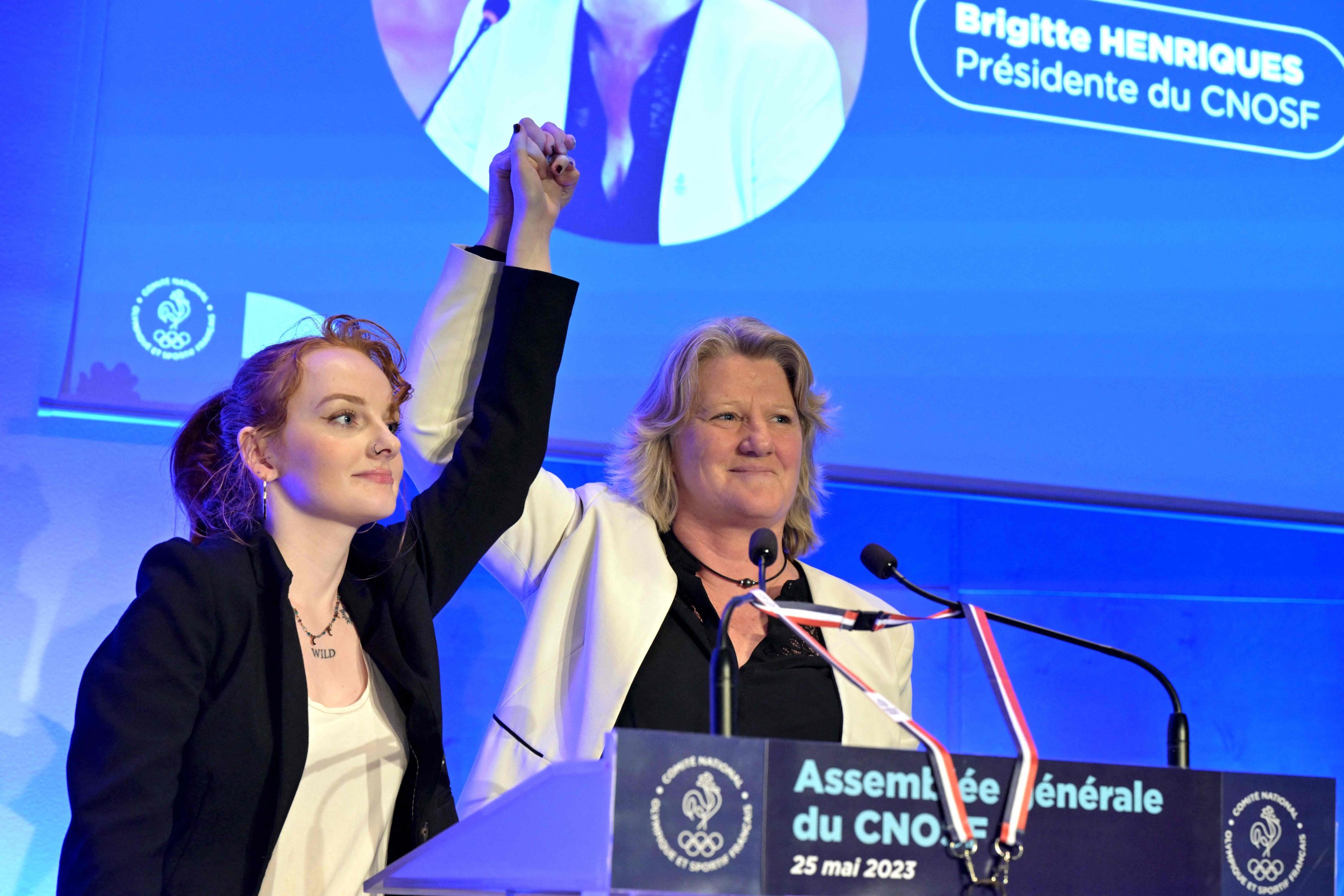Presiden Komite Olimpiade Prancis (CNOSF) Brigitte Henriques (kanan) memegang tangan salah satu putrinya dalam pelukannya selama Sidang Umum organisasi tersebut, Paris, Prancis, 25 Mei 2023. (Foto AFP)