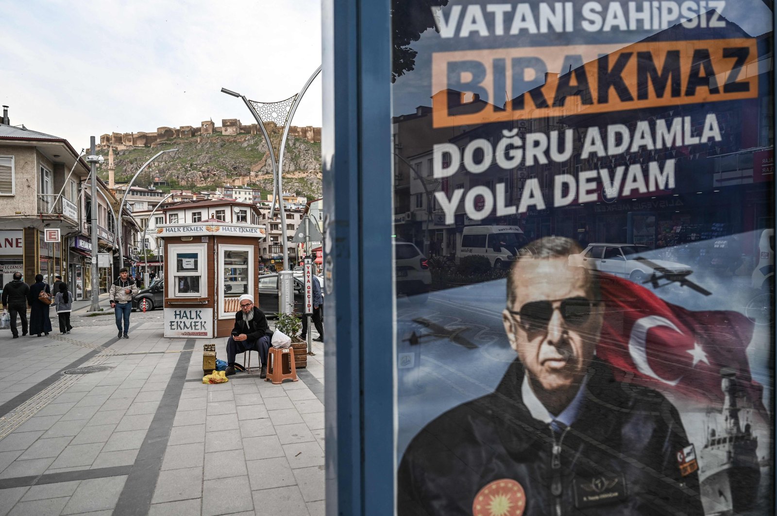 People sit next to an election banner of President Recep Tayyip Erdoğan at Bayburt city center, northeastern Türkiye, May 23, 2023. (AFP Photo)