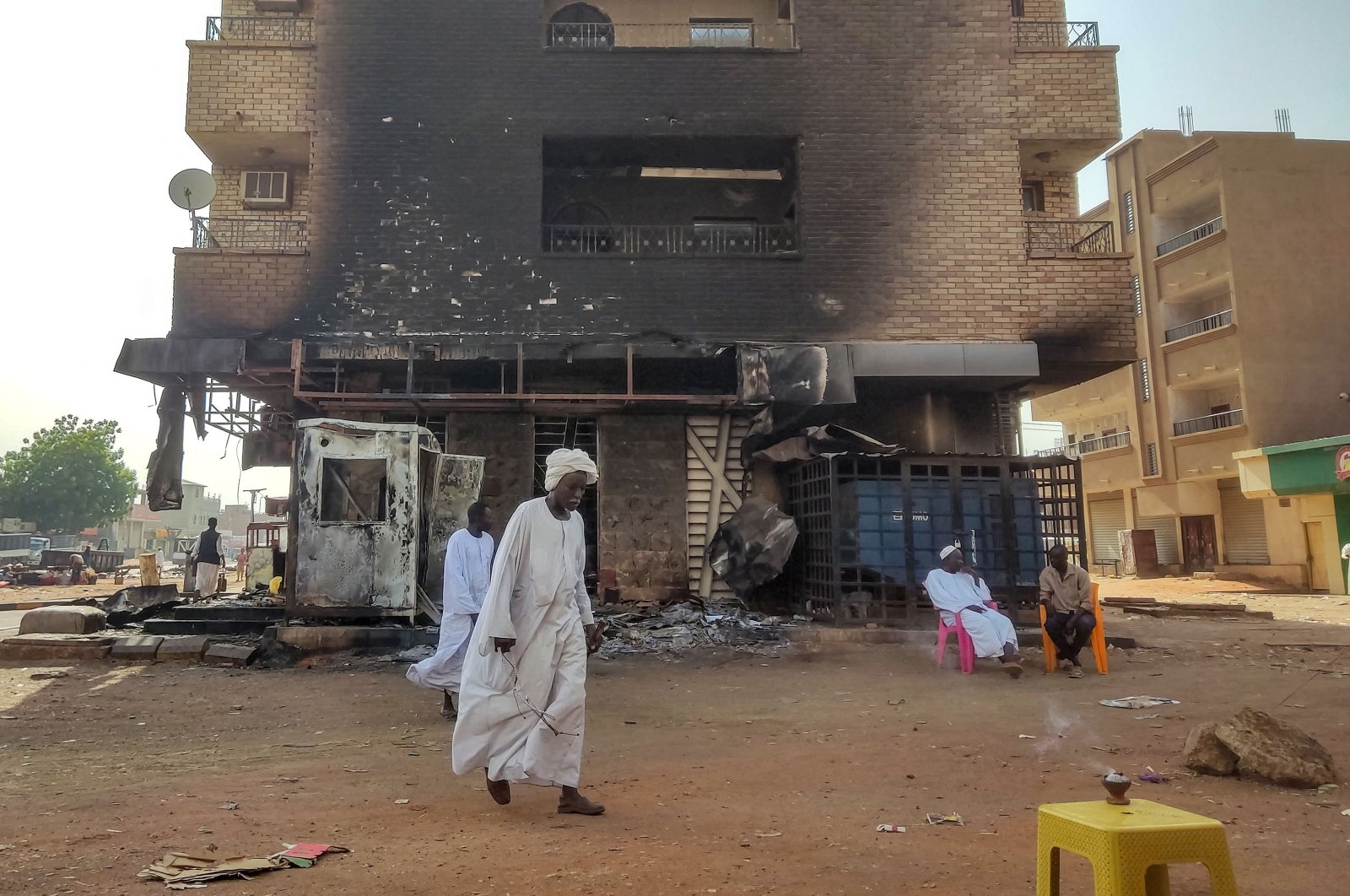 Men walk past others sitting outside a burn-down bank branch in southern Khartoum, Sudan, May 24, 2023. (AFP Photo)