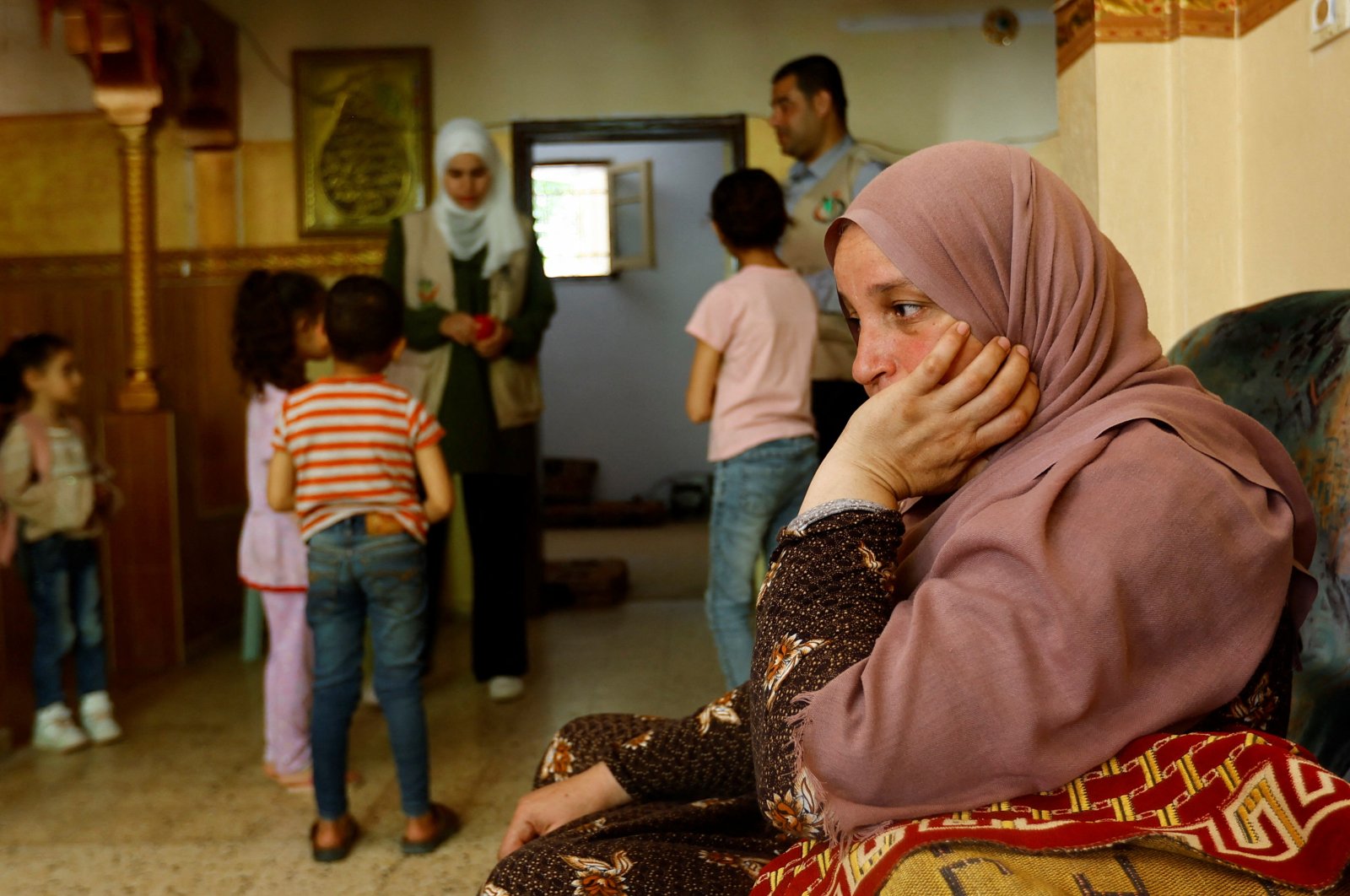 A Palestinian woman sits at her house, as a psychiatrists performs an activity with children, in Deir al-Balah, central Gaza Strip, May 16, 2023. (Reuters Photo)