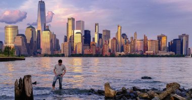 A man checks his footing as he wades through the Morris Canal Outlet in Jersey City as the sun sets on the lower Manhattan skyline of New York City, U.S., May 31, 2022. (AP Photo)