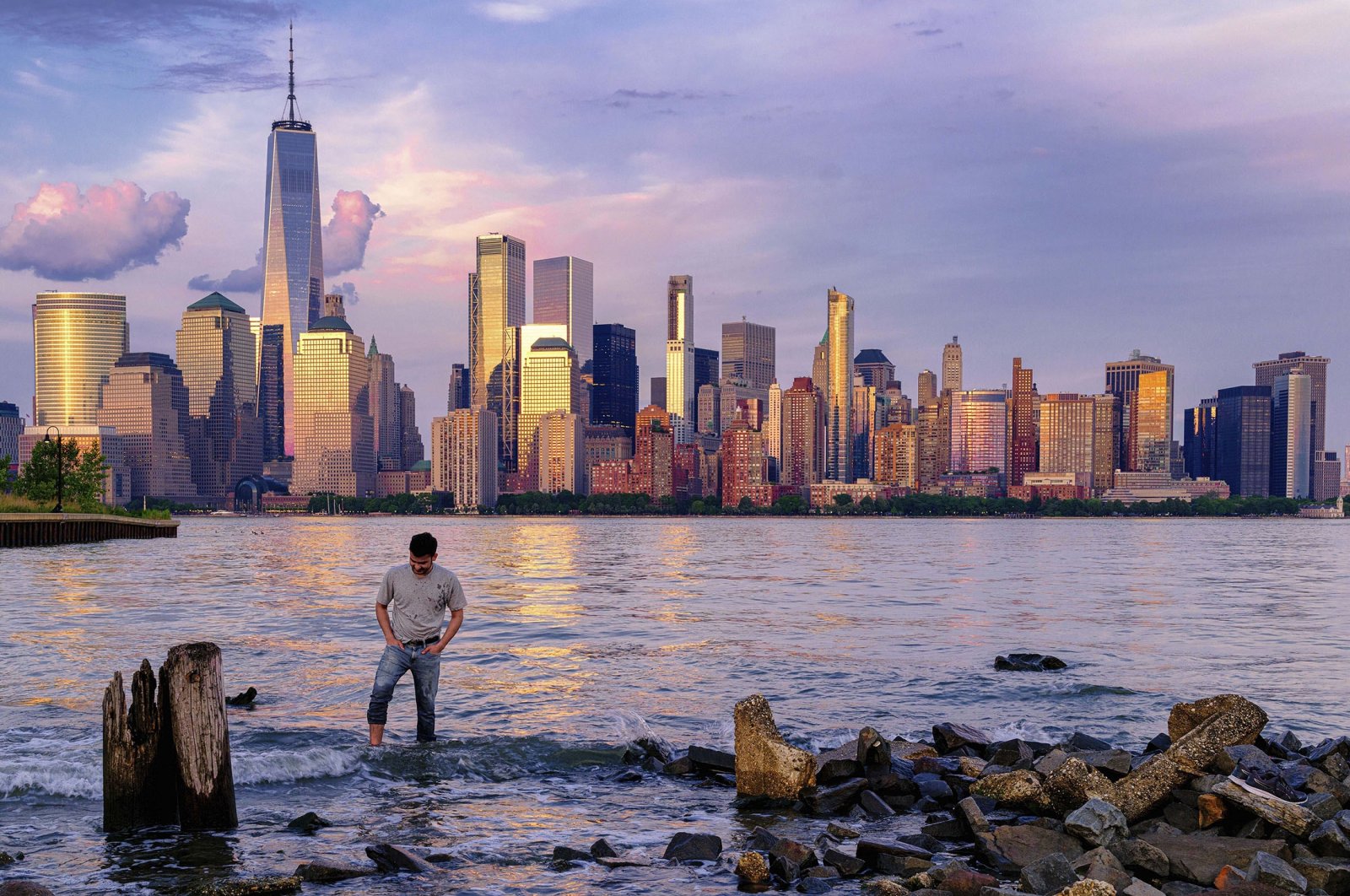 A man checks his footing as he wades through the Morris Canal Outlet in Jersey City as the sun sets on the lower Manhattan skyline of New York City, U.S., May 31, 2022. (AP Photo)