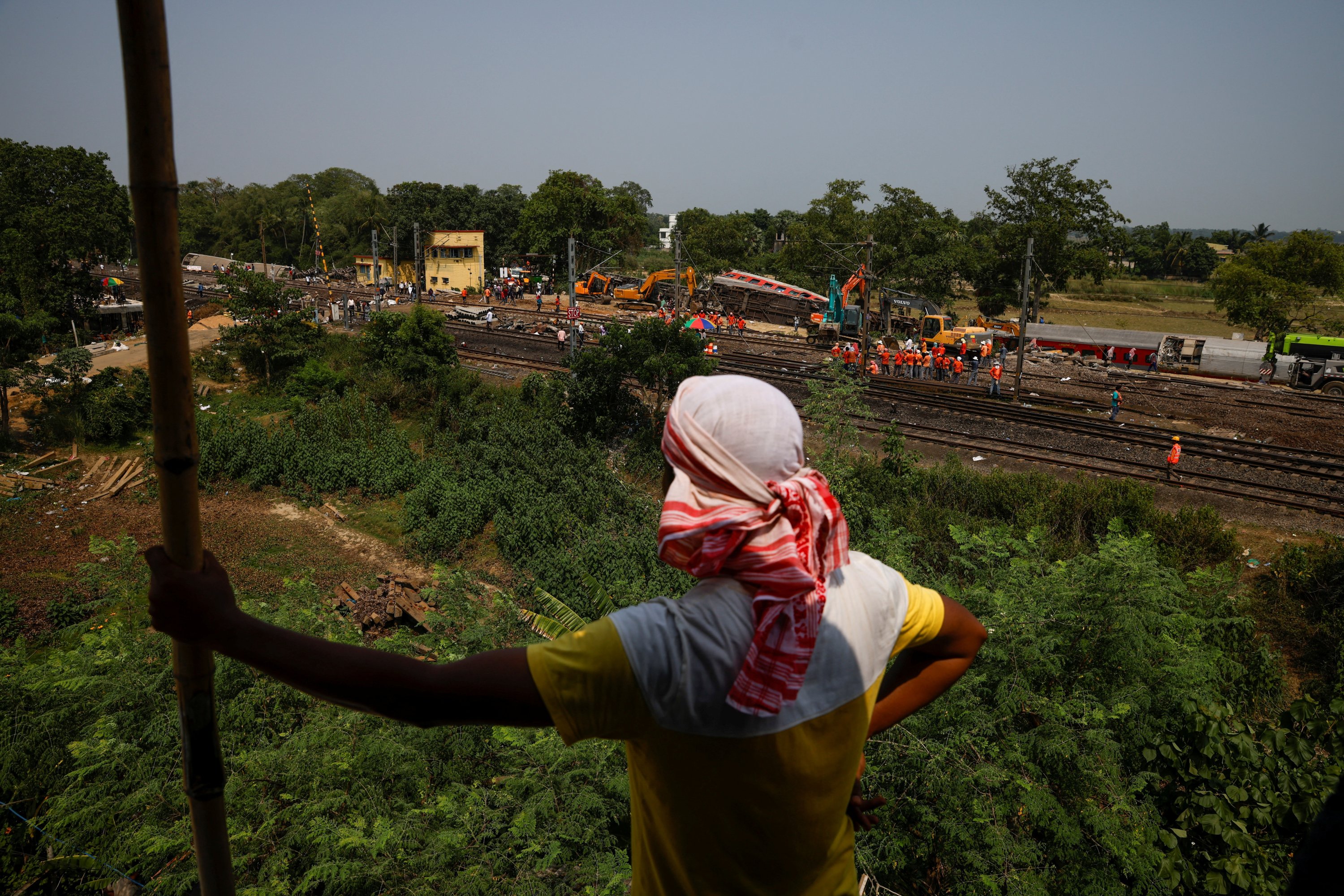 Seorang pria berdiri di atap sebuah rumah ketika dia melihat alat berat mengeluarkan gerbong yang rusak dari rel kereta api di lokasi tabrakan kereta api setelah kecelakaan di distrik Balasore di negara bagian timur Odisha, India, 4 Juni 2023. (Reuters Foto)