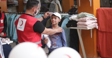 A Turkish Red Crescent worker hands out new clothes to a Syrian boy in Azaz, Syria, July 18, 2021. (AA Photo)