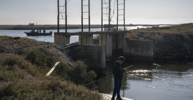 A boy fishes as police border guards on a boat patrol along the Evros River that forms a natural border between Greece and Türkiye, on Sunday, Oct. 30, 2022. (AP File Photo)