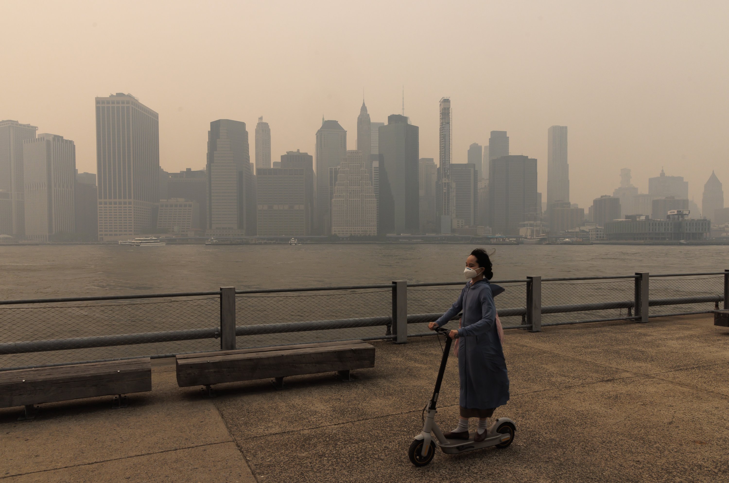Seseorang yang memakai masker dan mengendarai skuter melewati gedung-gedung di Manhattan yang lebih rendah terlihat melalui kabut asap, New York, AS, 7 Juni 2023. (Foto EPA)