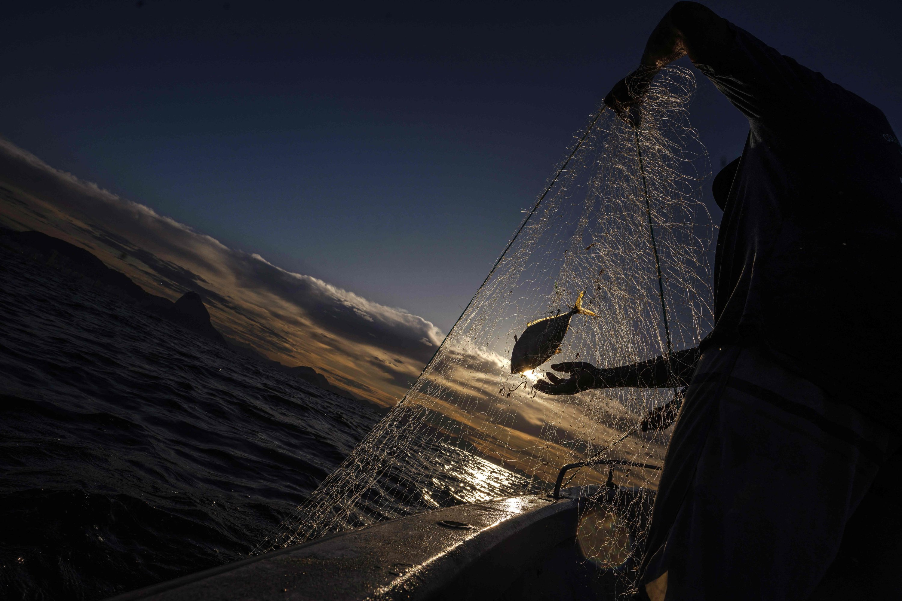 Nelayan menarik jaring dari air ke perahu mereka di dekat pantai Pantai Copacabana di Rio de Janeiro, Brasil, 23 Mei 2023. (Foto AFP)