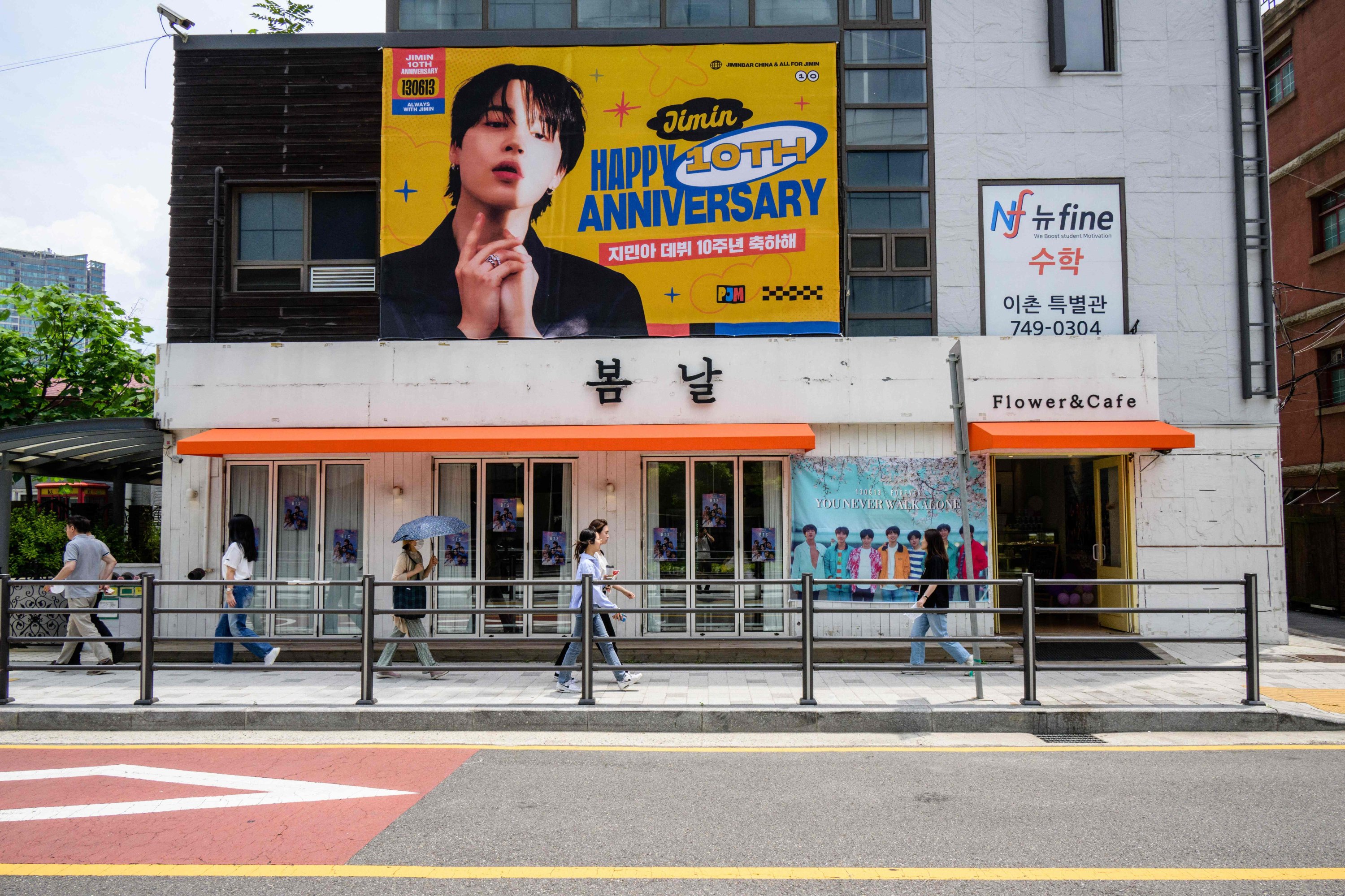 Pejalan kaki melewati poster perayaan 10 tahun megabintang K-pop BTS di luar sebuah kafe, Seoul, Korea Selatan, 12 Juni 2023. (AFP Photo)