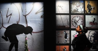 A visitor looks at a painting depicting a graffiti artist vomiting flowers made by British artist Banksy displayed during his solo show "CUT &amp; RUN: 25 years card labour" at the entrance of The Gallery Of Modern Art (GOMA), Glasgow, Scotland, June 15, 2023. (AFP Photo)