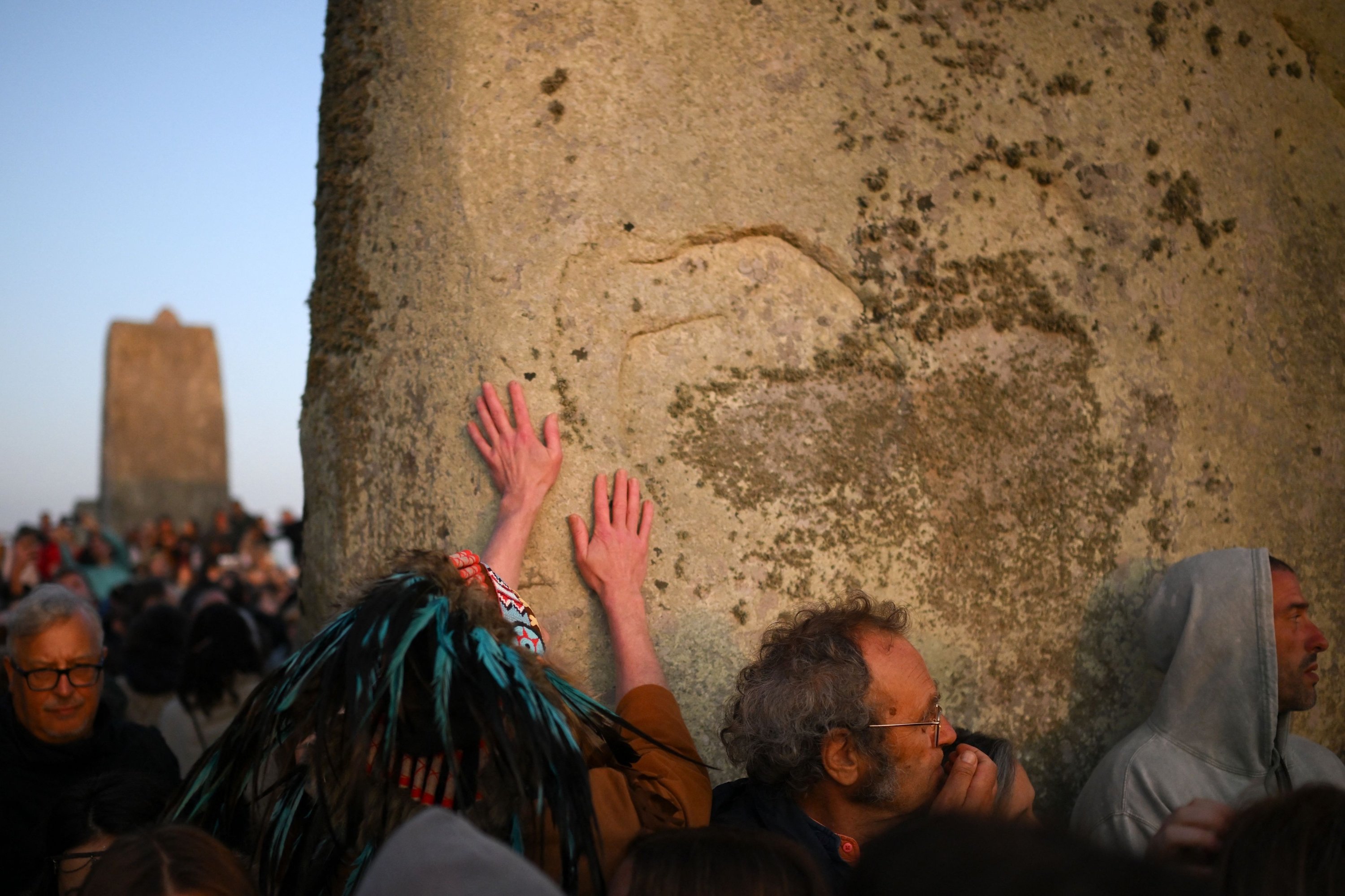 Orang-orang yang bersuka ria menyentuh batu saat mereka merayakan Summer Solstice saat matahari terbit di Stonehenge, dekat Amesbury, di Wiltshire, Inggris selatan, 21 Juni 2023. (AFP Photo)