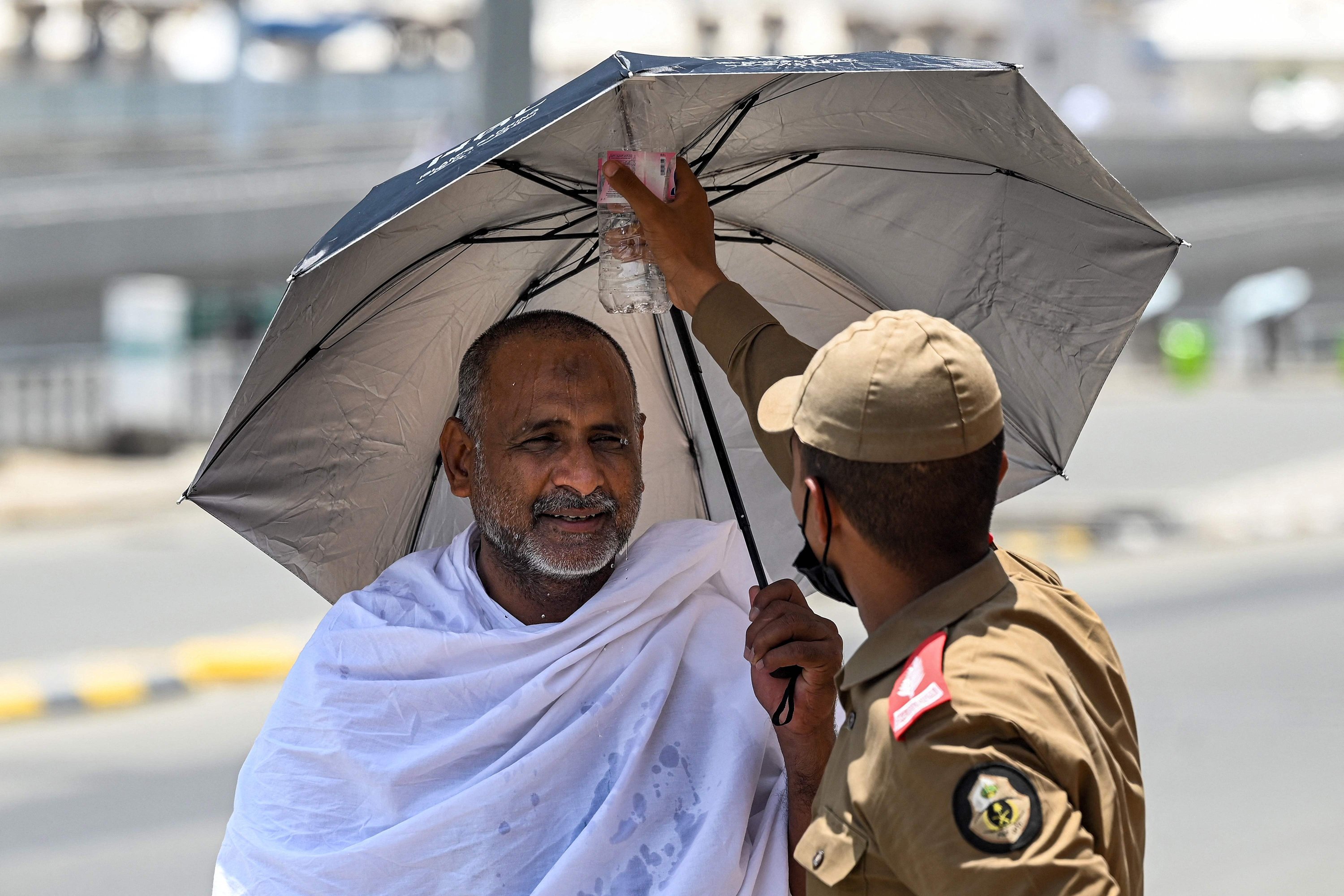 Seorang anggota keamanan menyemprotkan air ke seorang jamaah Muslim setibanya di Mina, Mekkah, Arab Saudi, 26 Juni 2023. (Foto AFP)