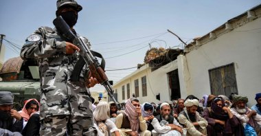 A Taliban security personnel stands guard next to prisoners waiting for release from the central prison in Kandahar, Afghanistan, June 27, 2023. (Photo by Sanaullah SEIAM / AFP)