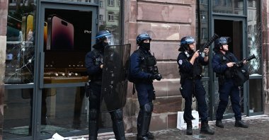 French police officers in riot gear stand guard and hold tear gas canister launchers next to the facade of a damaged Apple Store at Place Kleber, in Strasbourg, eastern France, on June 30, 2023. (AFP Photo)